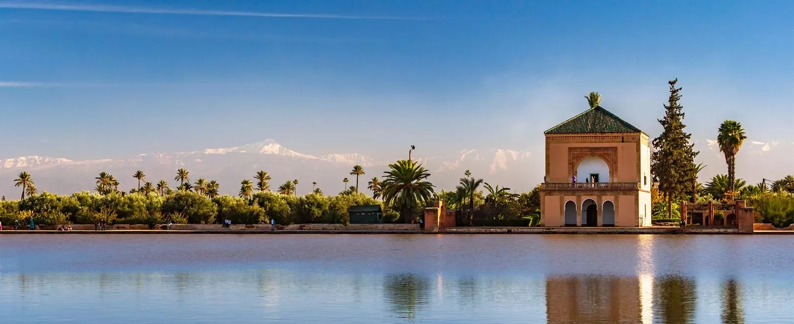Vue panoramique de Marrakech au Maroc, palmiers, remparts ocre et montagnes de l’Atlas en arrière-plan sous un ciel lumineux.