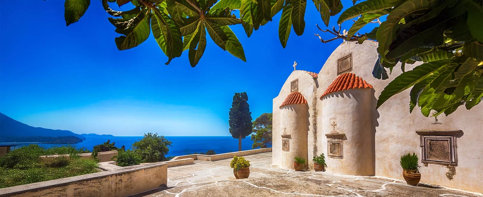 Chapelle blanche surplombant la mer en Crète, vue panoramique sur la côte et le bleu de la mer Égée par temps clair.