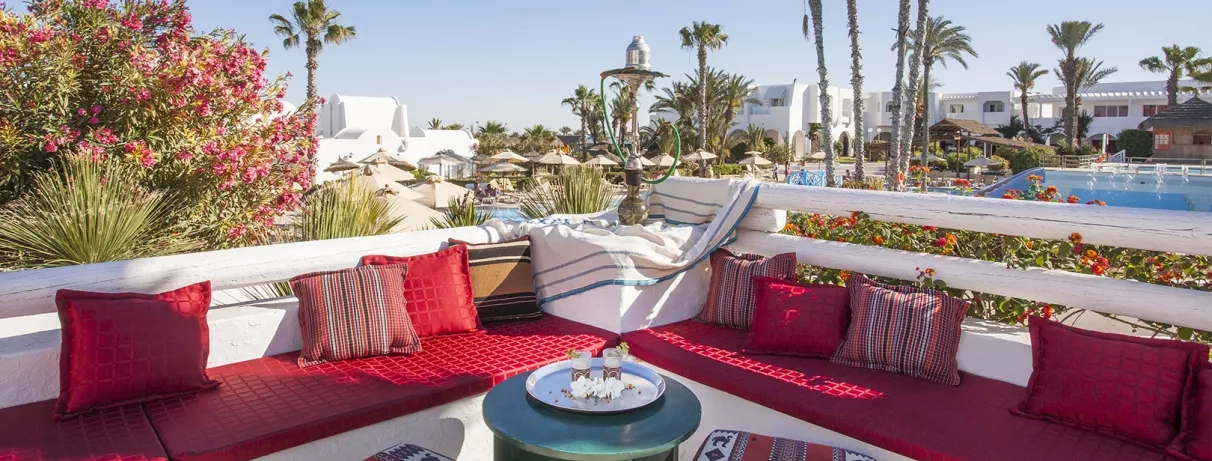 Terrasse traditionnelle avec chicha et coussins rouges offrant une vue sur les jardins du Mondi Club.