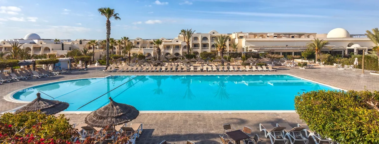 Grande piscine extérieure entourée de palmiers et de transats sous le soleil de Djerba, en Tunisie.