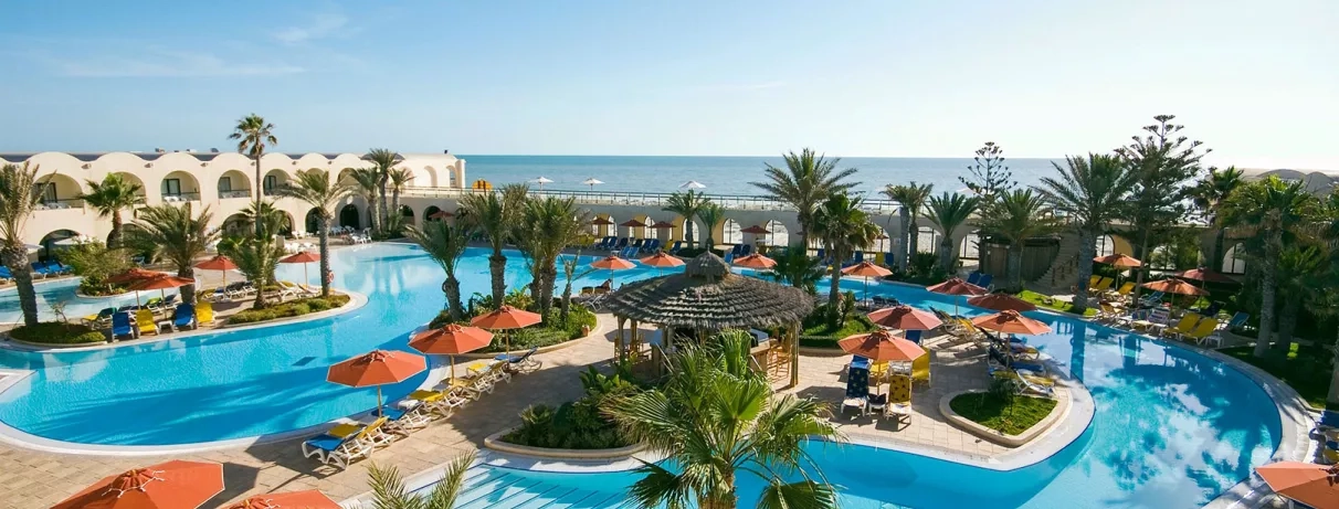 Vue panoramique sur les piscines extérieures et la mer Méditerranée au complexe hôtelier Djerba Beach.