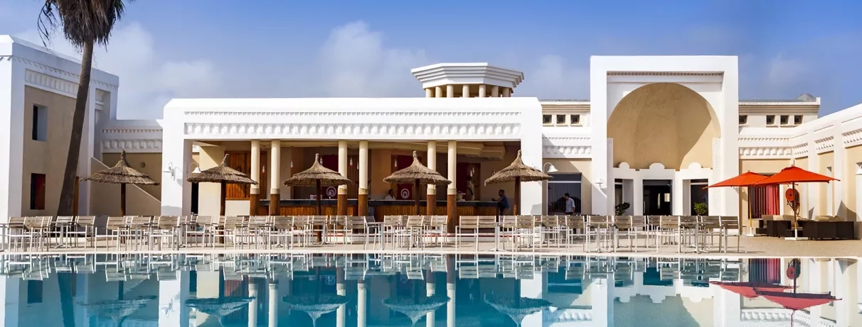 Façade élégante de l’hôtel donnant sur la piscine, avec un espace bar ombragé équipé de chaises hautes et de parasols