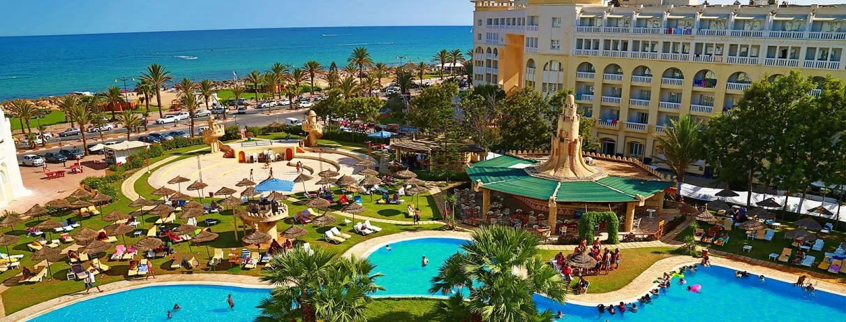 Vue générale de l’hôtel mettant en valeur la piscine extérieure, le bâtiment principal et la vue sur la plage.