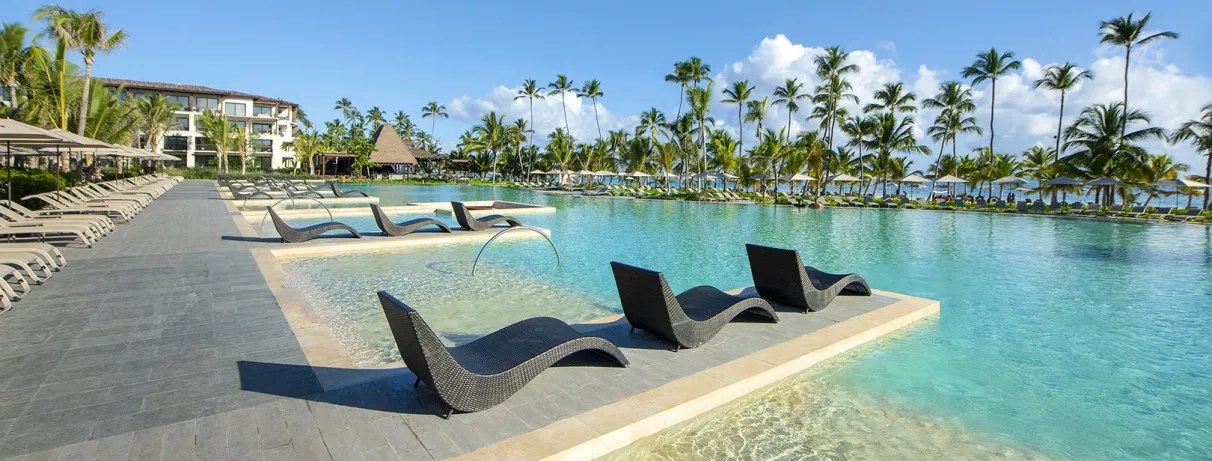 transats noirs dans piscine, palmiers, eau transparente, pieds dans l'eau