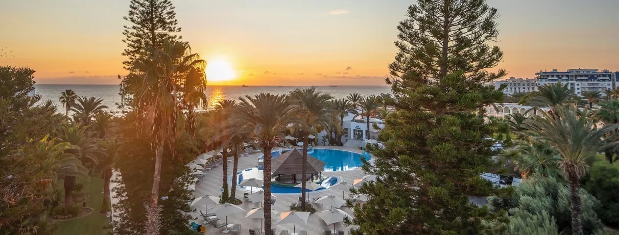 Vue panoramique du Marhaba Beach avec piscine et jardins sous un coucher de soleil en bord de mer à Monastir.