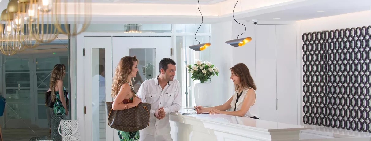 personnes à la réception discutant avec la réceptionniste, décoration blanche et épurée, vase blanc avec bouquet de fleurs