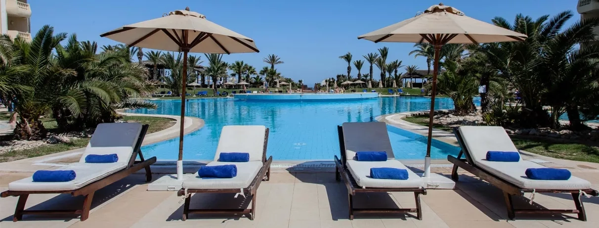 Transats avec serviettes bleues bordant une piscine azur sous le soleil, Royal Thalassa Monastir, vacances détente.