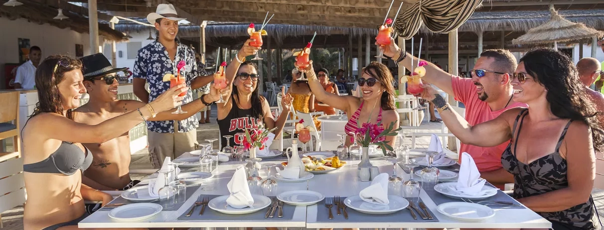 Clients joyeux trinquant avec des cocktails colorés au restaurant de plage de l'hôtel Seabel Rym Beach.