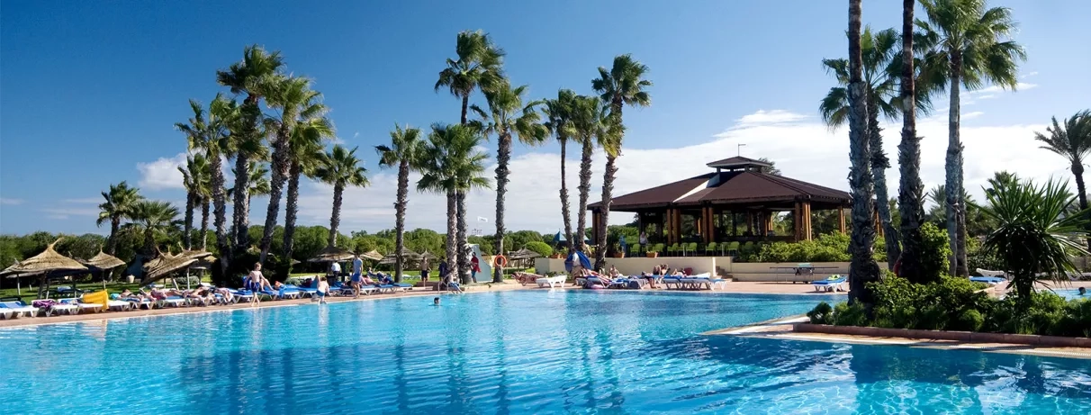 Piscine extérieure azur entourée de palmiers et transats sous le soleil au Sahara Beach Monastir.