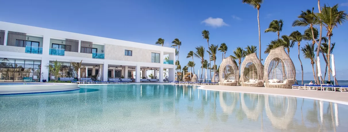 piscine, banquettes, palmiers, transats, ciel bleu, végétation luxuriante