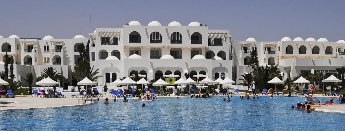 Grande piscine extérieure de l'hôtel avec vacanciers et architecture traditionnelle blanche pour un séjour en Tunisie.