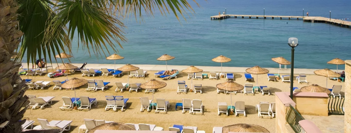 Une vue de la plage avec de nombreux transats face à la mer et à un ponton.