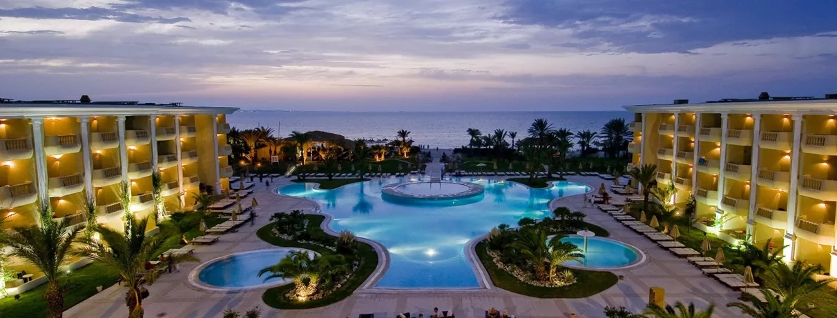 Vue nocturne illuminée des piscines et façades de l'hôtel luxe Royal Thalassa Monastir face mer.