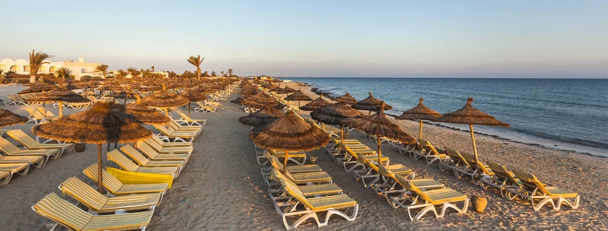 Rangées de transats et parasols en paille sur la vaste plage de sable au Seabel Rym Beach.