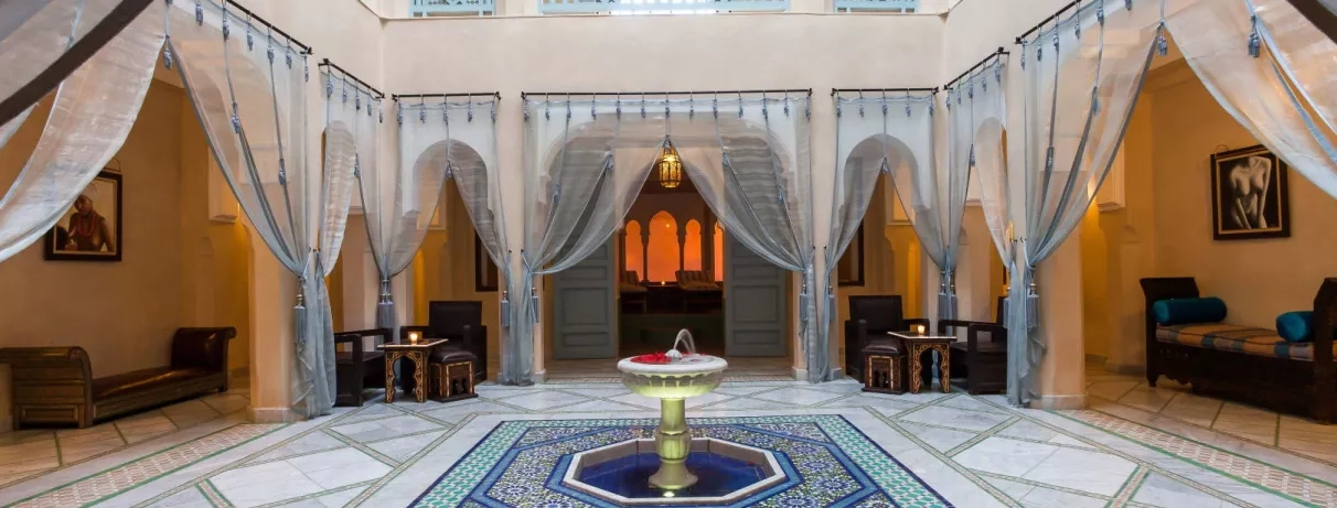 hall d'entrée, petite fontaine au centre de la pièce, grands rideaux gris, canapés et fauteuils style marocain