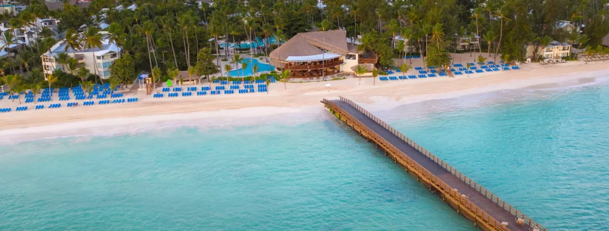 Plage avec ponton, sable, eau claire, transats bleus, plusieurs piscines, végétation