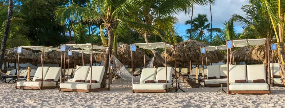 Transats confortables et auvents blancs, plage de sable blanc, palmiers cocotiers, ciel bleu