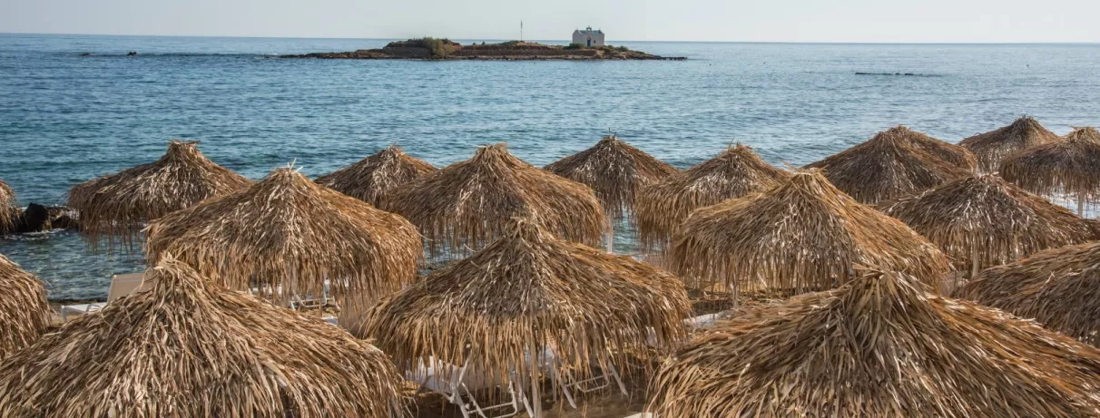 plage, parasols paillotes, transats blancs, pieds dans l'eau, vue sur petite ile en face et sa chapelle