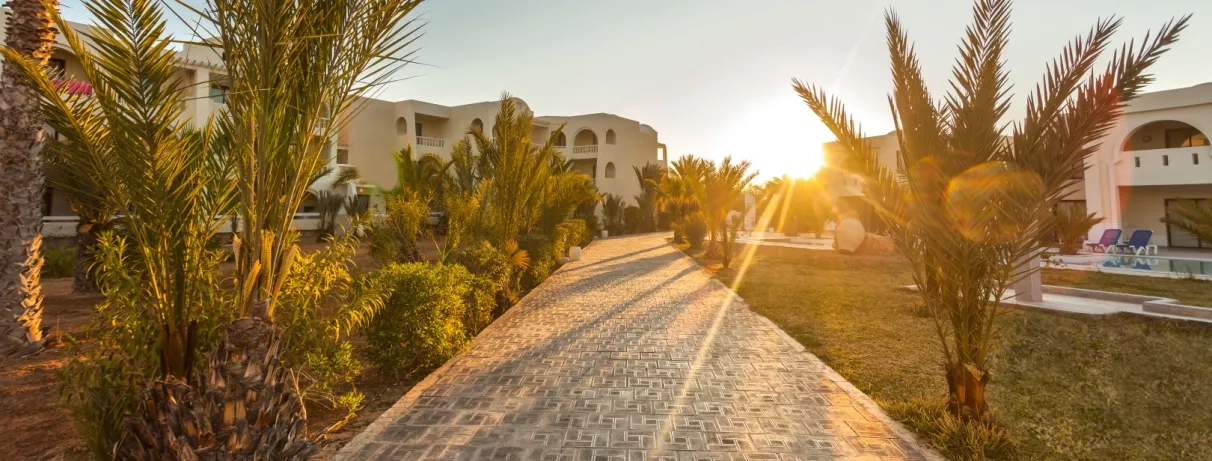 Allée pavée bordée de palmiers au coucher du soleil à l'hôtel César Thalasso de Djerba, Tunisie.