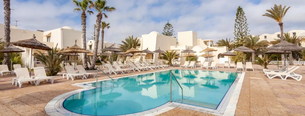Piscine de détente entourée de transats et parasols en paille au César Thalasso, séjour balnéaire Djerba.
