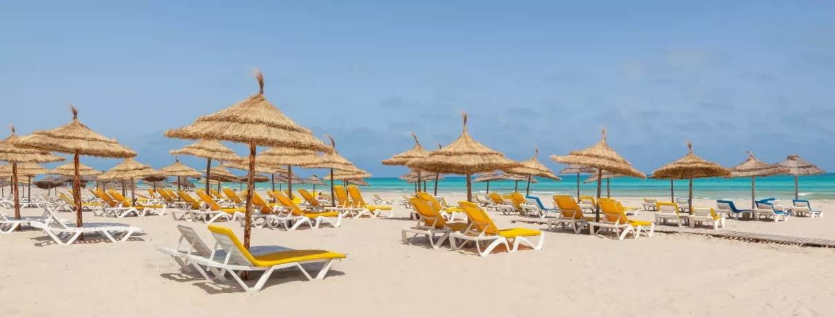 Plage de sable fin et parasols traditionnels face à la mer Méditerranée à Djerba, vacances Tunisie.