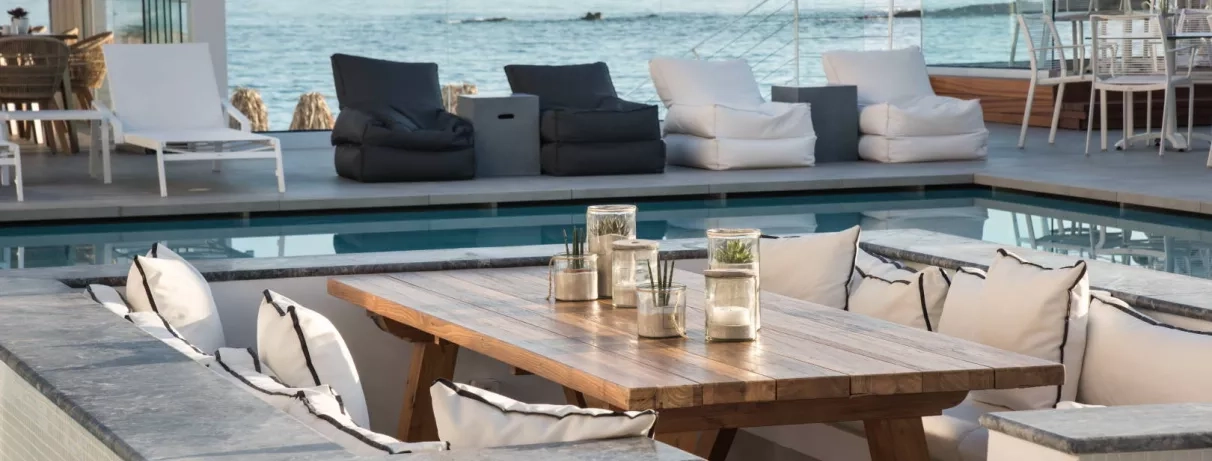 bar de la piscine, gros fauteuils blancs et noirs autour, bougies et petites plantes posées sur la table basse, vue sur la mer
