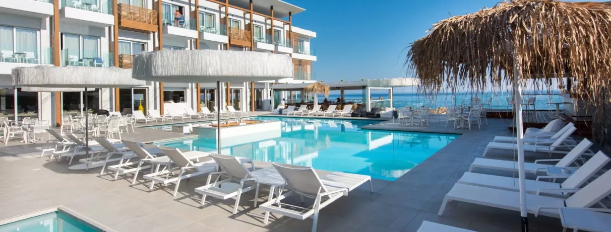 piscine avec transats, parasols, pieds dans l'eau, hôtel avec balcons couleur bois