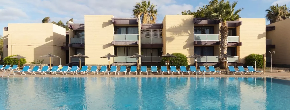 Une vue d'un bâtiment à plusieurs étages avec balcons, situé juste au bord d'une piscine.