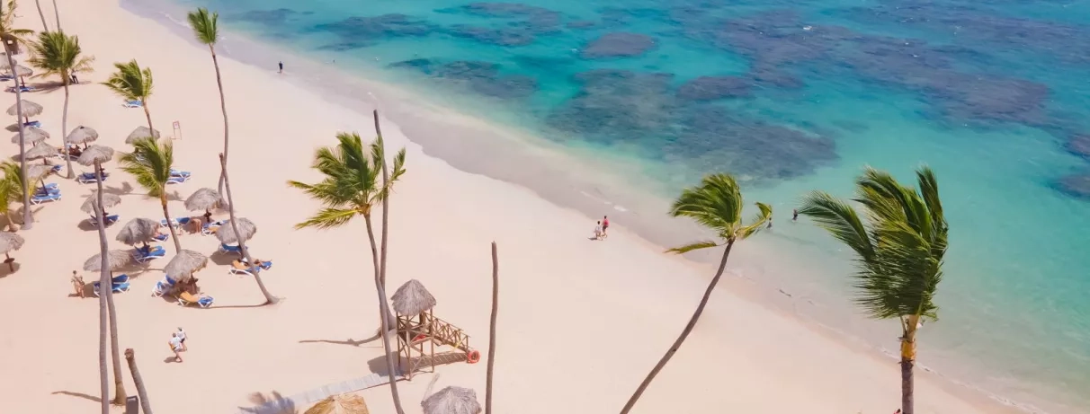 plage de sable blanc, eau turquoise, palmiers, transats bleus et parasols