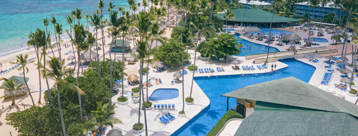 piscines, palmiers, transats bleus, parasols, pieds dans l'eau, cocotiers, plage de sable
