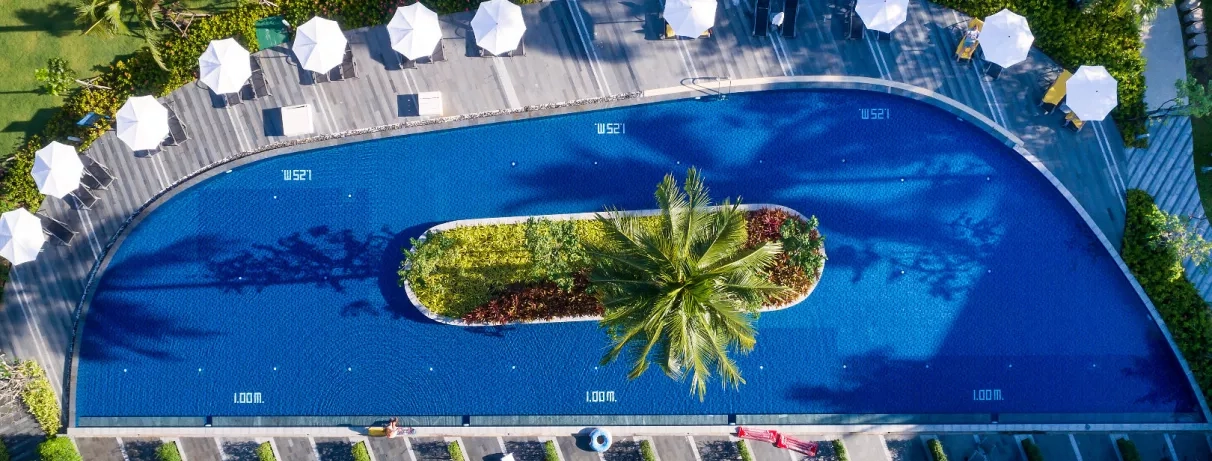 Une large piscine entourée de palmiers et de jardins tropicaux au coucher du soleil.