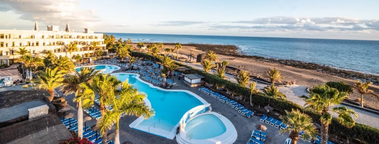 Un panorama ensoleillé montrant une piscine, nichée entre des bâtiments d'hôtel et la mer.