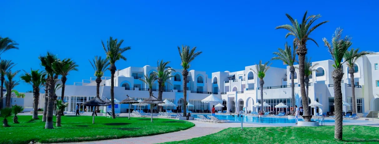 Grande piscine extérieure entourée de palmiers et architecture blanche typique de l'hôtel Al Jazira à Djerba.