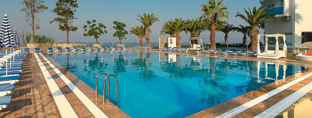 Une grande piscine à débordement, bordée de palmiers sous un ciel bleu.