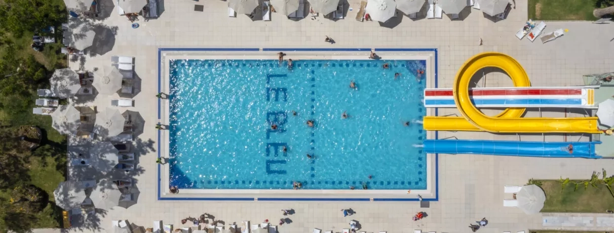 Une vue aérienne d'une piscine équipée d'un grand toboggan et de parasols.
