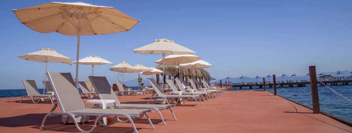 Une rangée de transats et de parasols installés sur une terrasse en bois face à la mer.