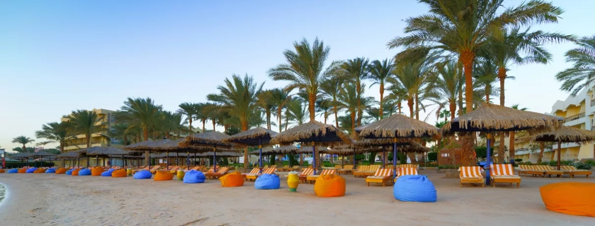 plage avec transats, parasols, poufs colorées, palmiers, bâtiment de l'hôtel