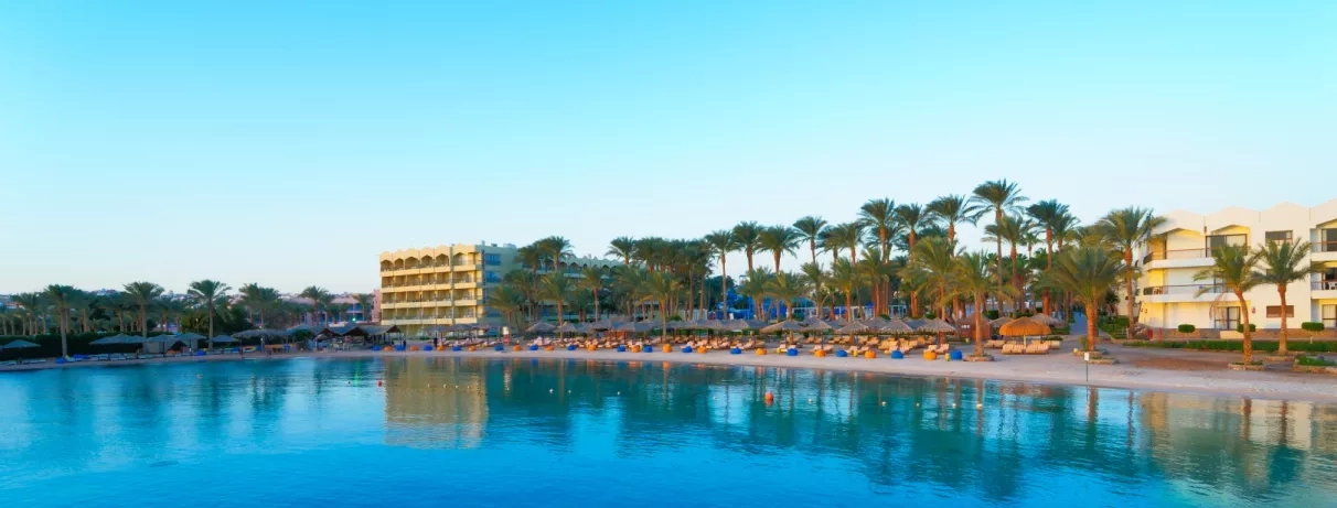 vue panoramique sur façade côté mer  avec transats, parasols, poufs colorées, palmiers, bâtiment de l'hôtel