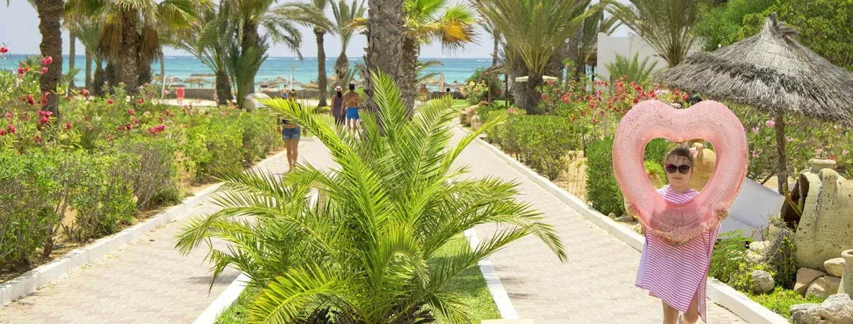 Allée fleurie et palmiers menant à la plage de sable fin au Mondi Club Seabel Aladin.