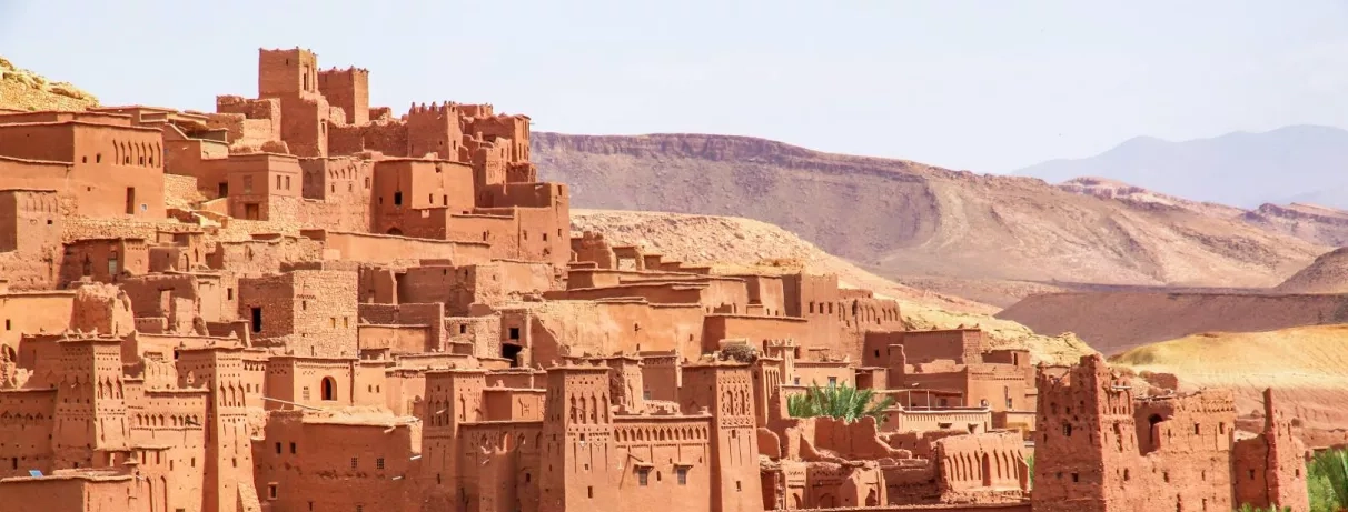Kasbah, un ksar ancestral aux murs de terre s'élève en gradins devant des montagnes désertiques.