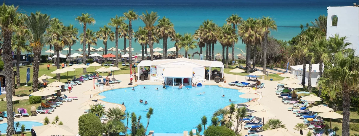 Vue en hauteur sur la piscine extérieure, offrant un panorama dégagé avec la plage et la mer en toile de fond