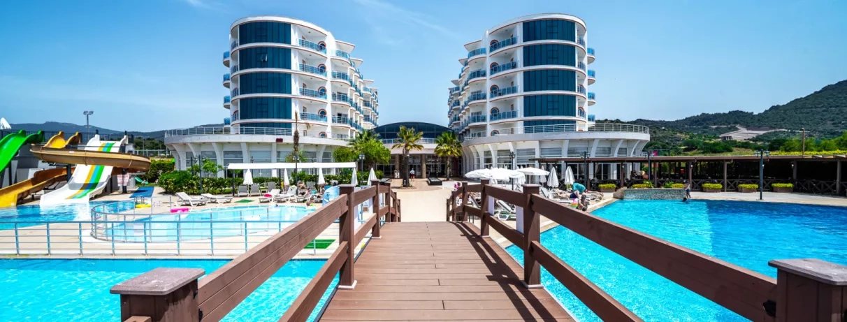 Un ponton en bois mène vers deux bâtiments d'hôtel modernes entourés de grandes piscines bleues.