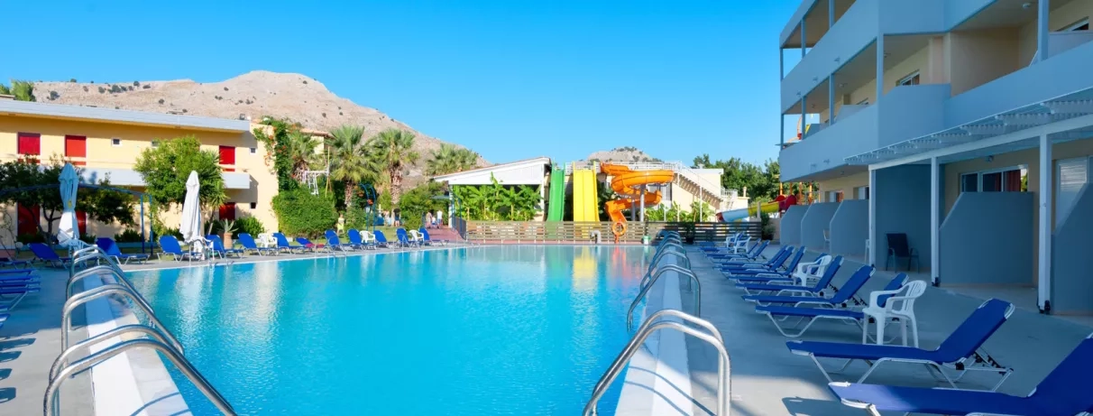 vue d'ensemble piscine aquapark 3 toboggans vert jaune orange montagne transats bleus bâtiments de l'hôtel