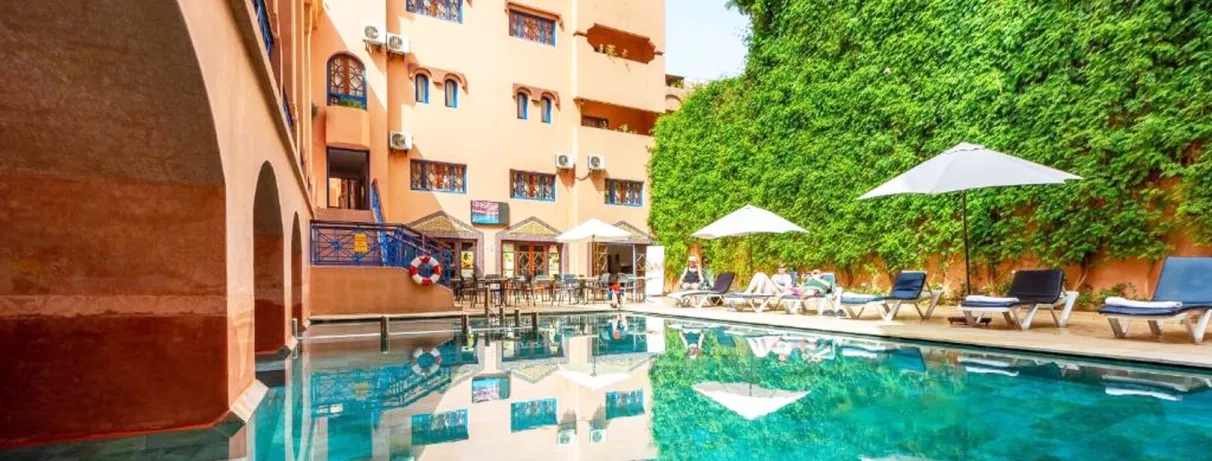 Une vue sur la piscine de l'hôtel, encadrée par un bâtiment moderne aux murs ocre et un grand mur végétal.