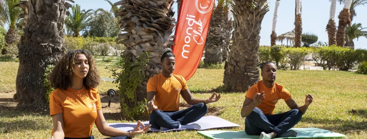 Un groupe d'animateurs pratiquant le yoga en plein air sur des tapis.