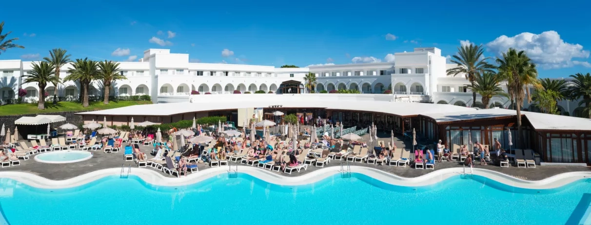 Une vue panoramique d'une grande piscine, bordée de transats devant l'hôtel.