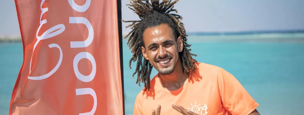 Animateur souriant devant la mer Rouge turquoise, séjour club tout compris au Stella Gardens Resort, Égypte.