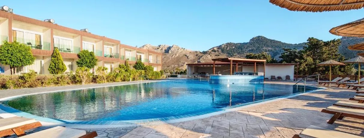 piscine transats, bâtiments hôtel un étage avec balcons, montagnes en arrière-plan, ciel bleu