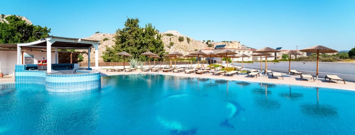 piscine avec dauphins au fond, pool bar couvert, transats et parasols, arbres et montagnes
