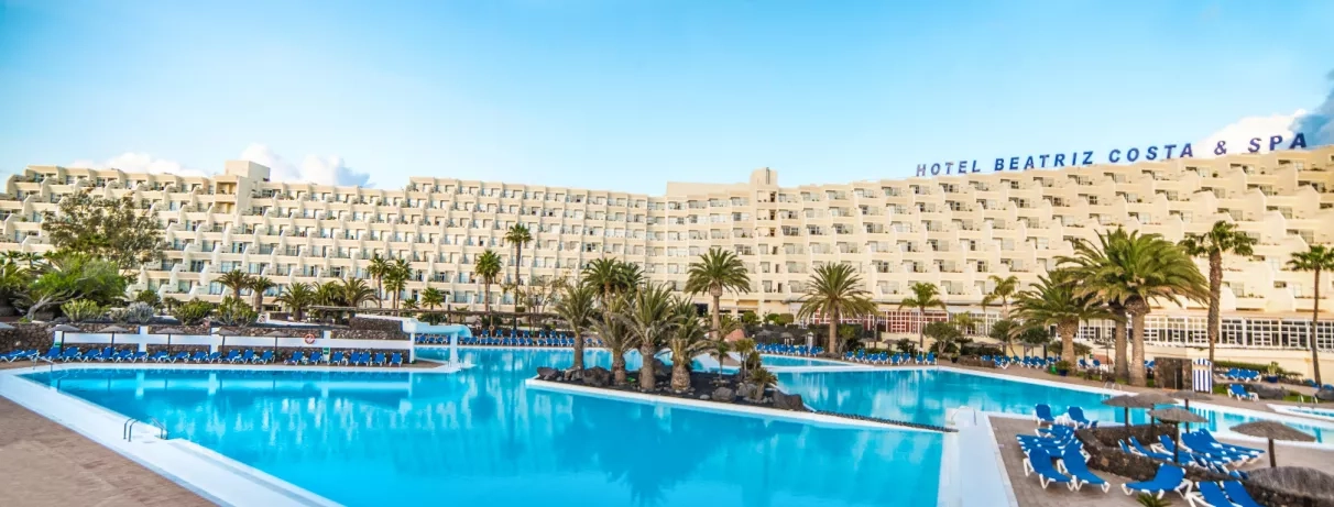 Une vue d'ensemble d'une grande piscine bordée de palmiers, avec un imposant complexe hôtelier.